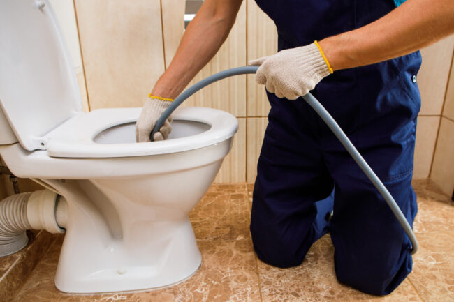 plumber unclogging blocked toilet with hydro jetting at home bathroom Is Hydro Jetting Worth It